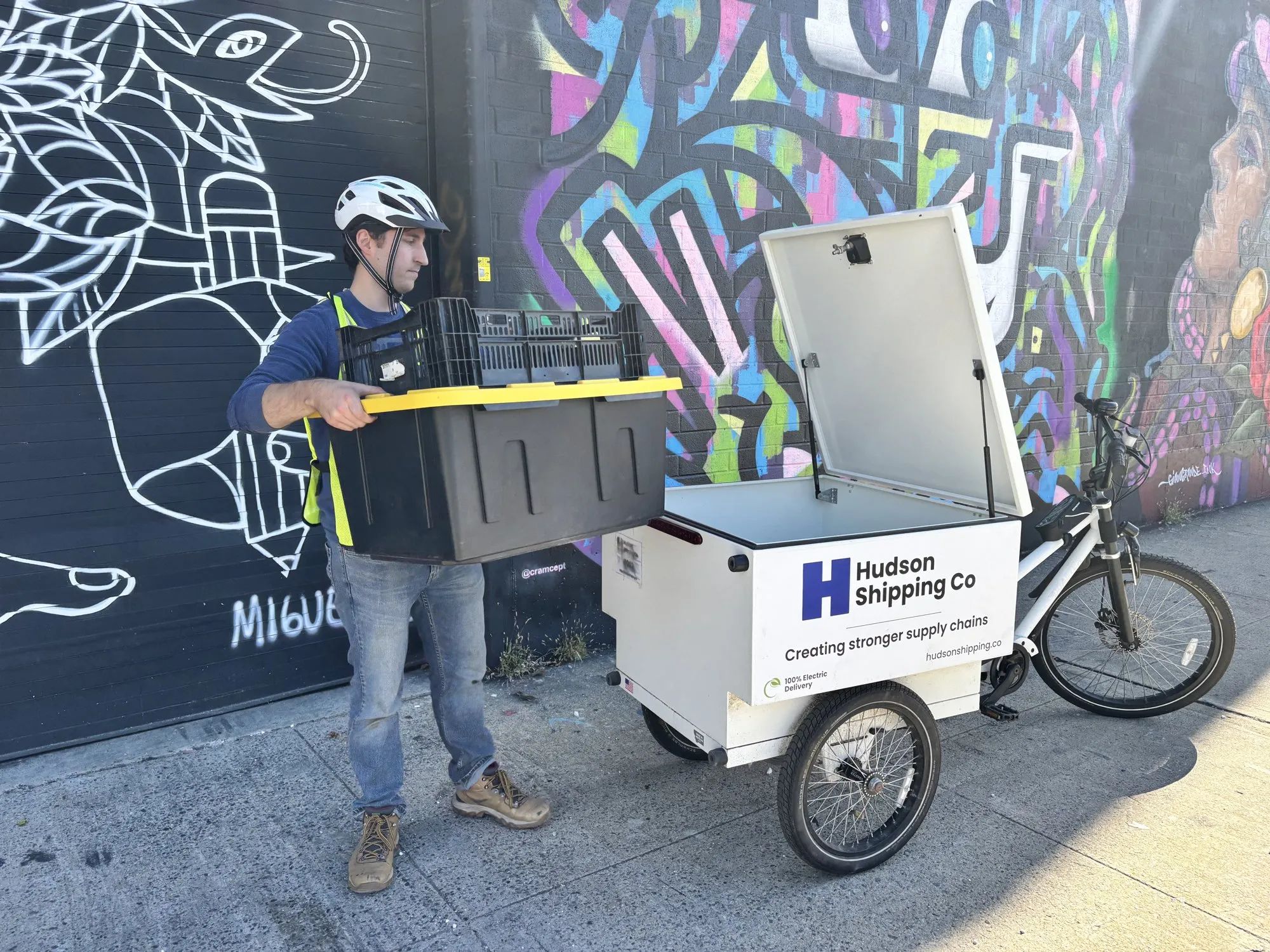 Courier carrying a tote next to the enclosed Hudson Shipping Co cargo bike